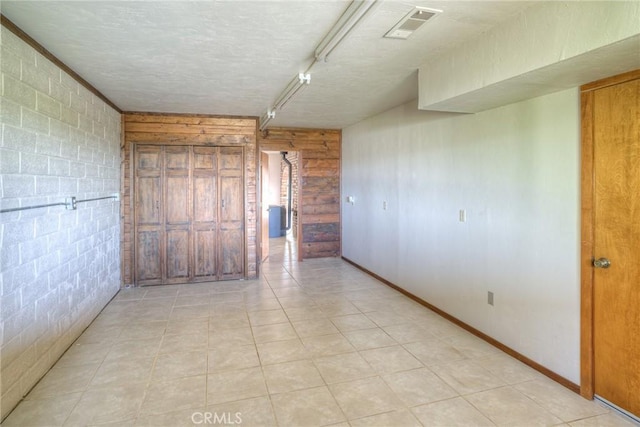 empty room with rail lighting, a textured ceiling, visible vents, and wooden walls