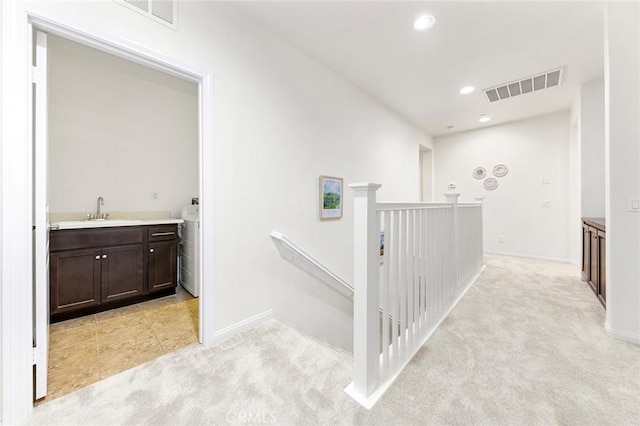 hall with visible vents, baseboards, light carpet, and an upstairs landing