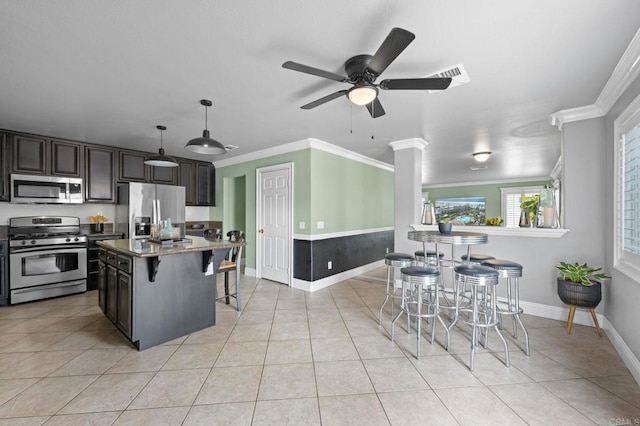 kitchen with stainless steel appliances, ornamental molding, baseboards, a breakfast bar area, and ceiling fan