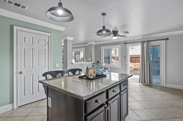 kitchen with a center island, visible vents, ornamental molding, ceiling fan, and light tile patterned floors