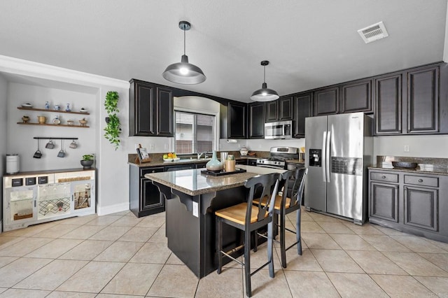 kitchen featuring stainless steel appliances, visible vents, light tile patterned floors, a kitchen island, and dark stone counters