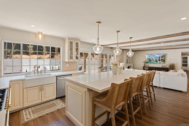 kitchen with a sink, cream cabinetry, open floor plan, stainless steel dishwasher, and wood finished floors