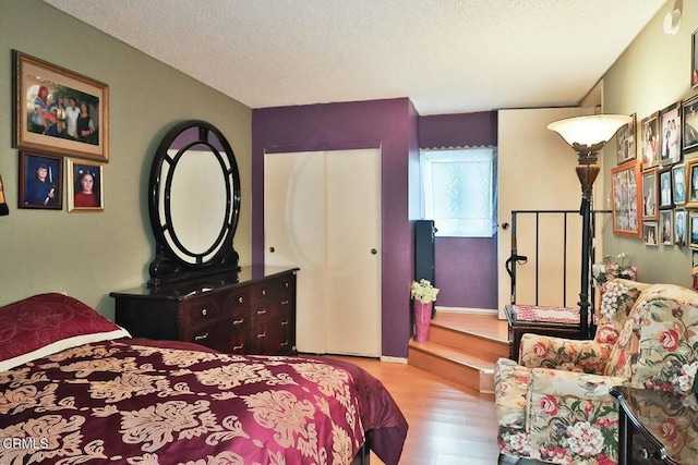 bedroom with wood finished floors, a textured ceiling, baseboards, and a closet