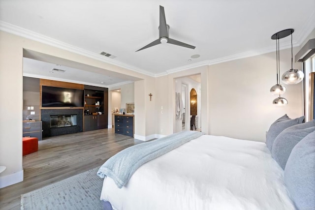 bedroom with a large fireplace, ornamental molding, wood finished floors, and visible vents