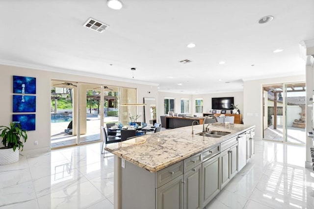 kitchen with a sink, visible vents, light stone countertops, an island with sink, and ornamental molding