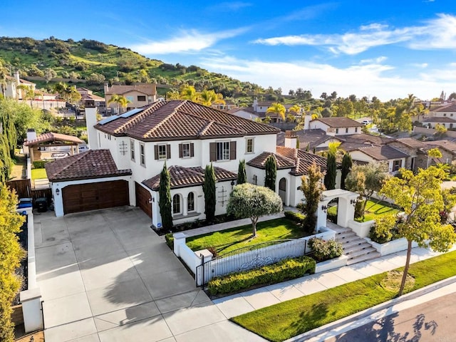 view of front facade with a fenced front yard, a tiled roof, a residential view, driveway, and a garage