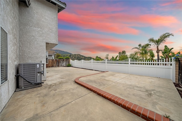 patio terrace at dusk with a fenced backyard and central AC unit