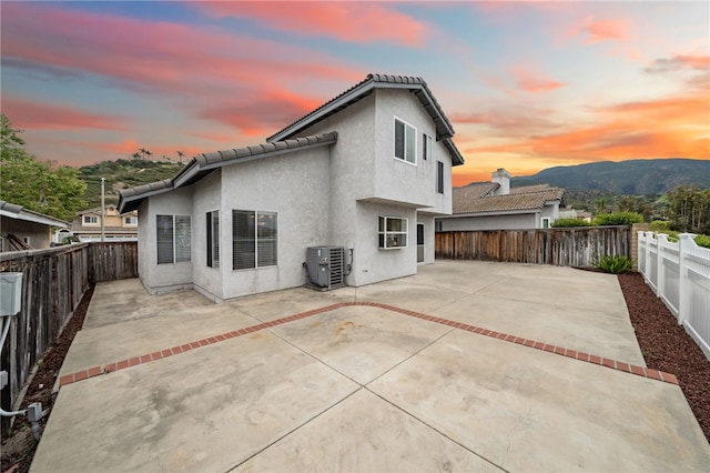 back of property at dusk with central air condition unit, a fenced backyard, and stucco siding