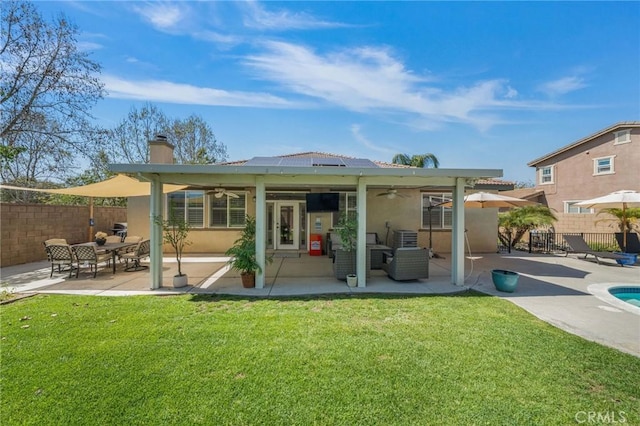 rear view of house featuring ceiling fan, a lawn, a chimney, roof mounted solar panels, and fence