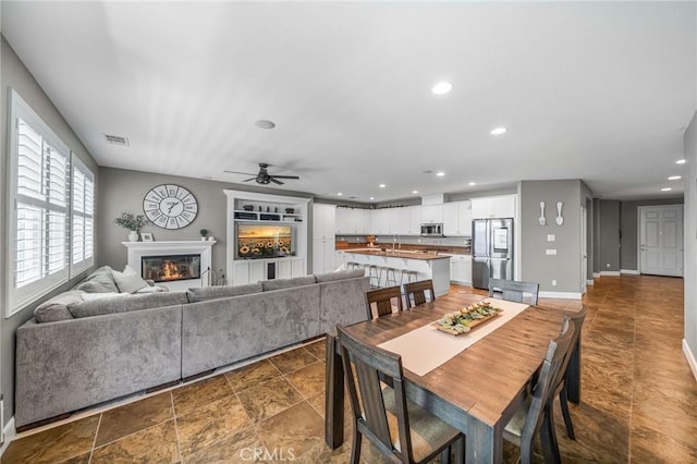 dining room featuring recessed lighting, a glass covered fireplace, a ceiling fan, visible vents, and baseboards