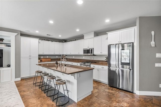 kitchen featuring recessed lighting, a breakfast bar, stainless steel appliances, a sink, and white cabinetry