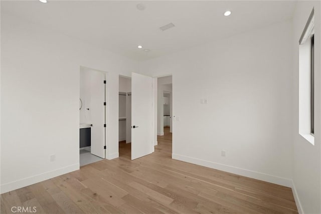 unfurnished bedroom featuring light wood finished floors, baseboards, recessed lighting, and a walk in closet