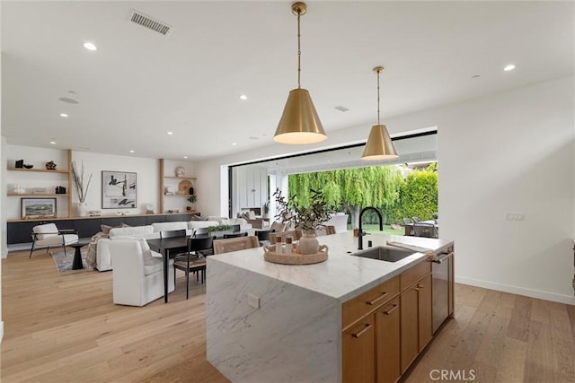 kitchen with a sink, a center island with sink, light wood-type flooring, visible vents, and decorative light fixtures