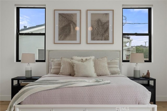 bedroom featuring baseboards, wood finished floors, and multiple windows