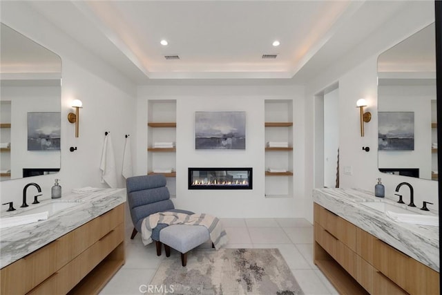 1311 18th St, Manhattan Beach, CA 90266 - bathroom featuring a glass covered fireplace, built in features, two vanities, a tray ceiling, and tile patterned flooring