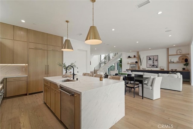 kitchen with a sink, light wood-type flooring, open floor plan, visible vents, and an island with sink