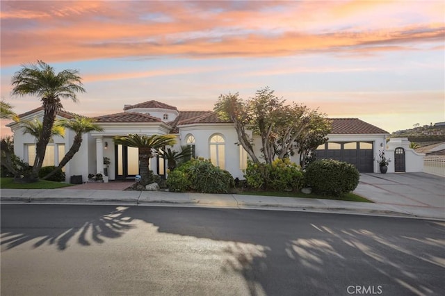 mediterranean / spanish-style home with an attached garage, stucco siding, driveway, and a tile roof