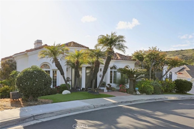 mediterranean / spanish house with a chimney, a front lawn, and stucco siding