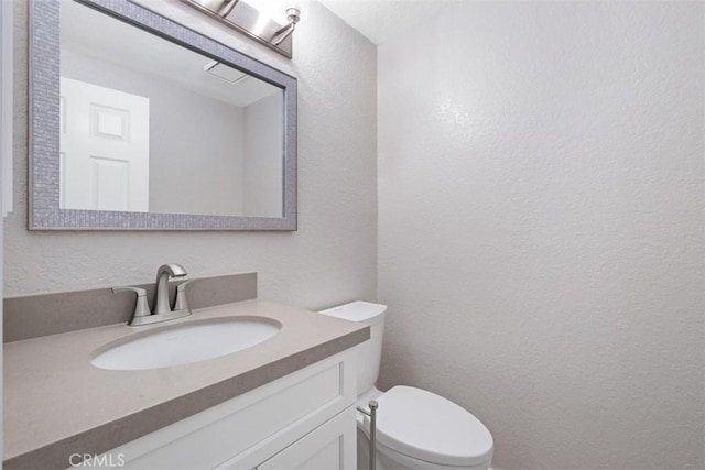 half bathroom with a textured wall, toilet, and vanity