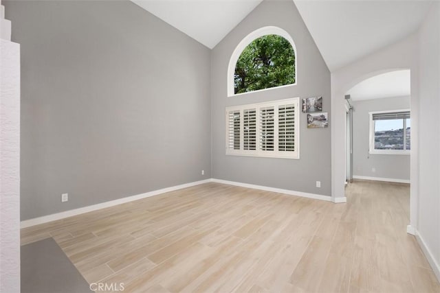 empty room with high vaulted ceiling, baseboards, arched walkways, and light wood-type flooring
