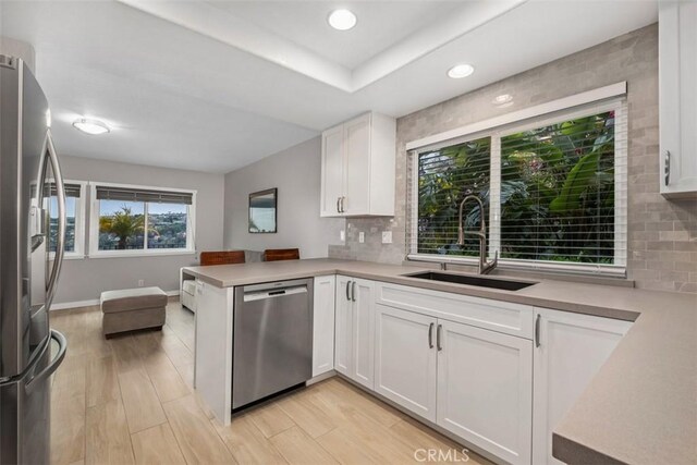 kitchen featuring white cabinets, appliances with stainless steel finishes, decorative backsplash, and a sink