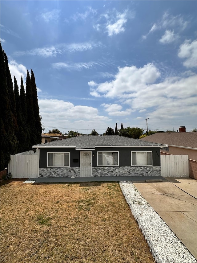 view of front of home featuring a front yard, fence, stone siding, and stucco siding