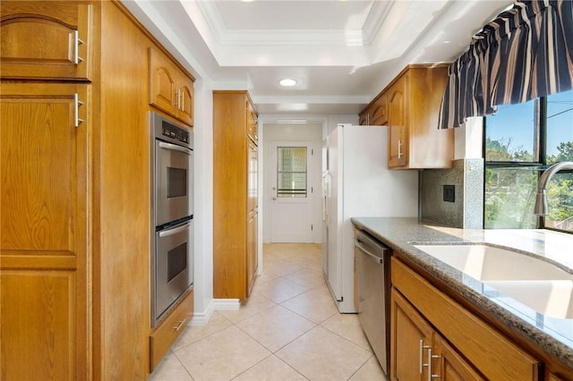 kitchen with brown cabinetry, stainless steel appliances, light stone counters, and a sink