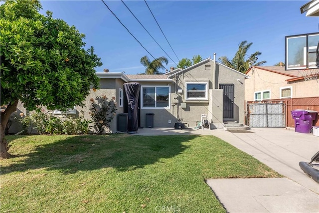 rear view of property featuring fence, a lawn, a gate, and stucco siding