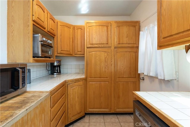 kitchen featuring stainless steel microwave, backsplash, tile countertops, and dishwashing machine
