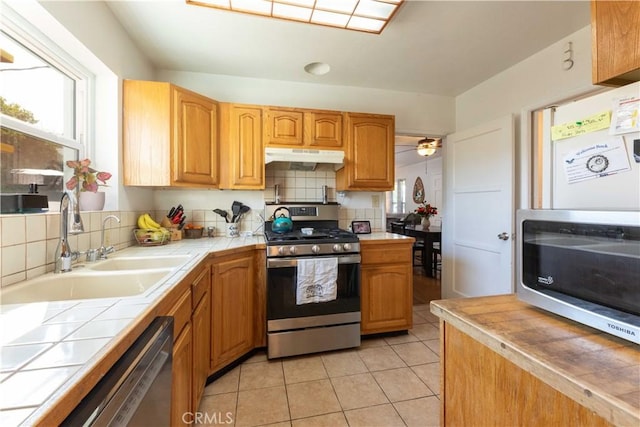 kitchen featuring tile counters, under cabinet range hood, a wealth of natural light, and appliances with stainless steel finishes