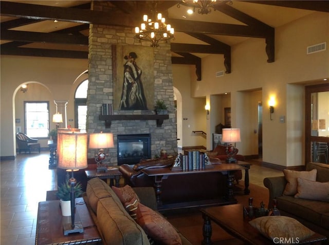 living area featuring visible vents, beam ceiling, baseboards, a stone fireplace, and arched walkways