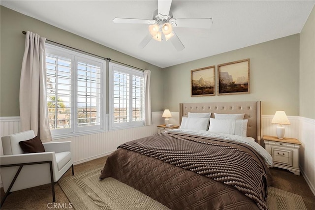 carpeted bedroom featuring a ceiling fan and wainscoting