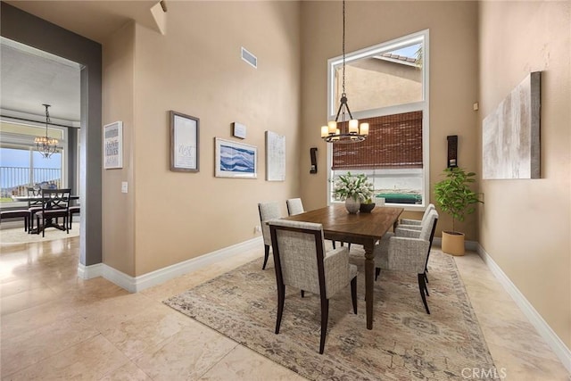 dining area featuring a towering ceiling, visible vents, a notable chandelier, and baseboards