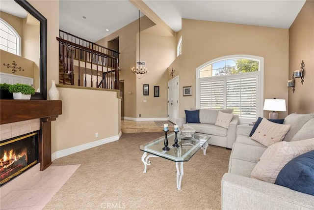 living area with stairway, a chandelier, a tiled fireplace, a high ceiling, and carpet flooring
