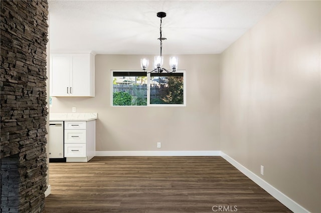 unfurnished dining area featuring an inviting chandelier, dark wood-type flooring, and baseboards