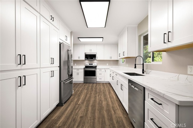 kitchen with light stone counters, a sink, stainless steel appliances, white cabinetry, and dark wood-style flooring
