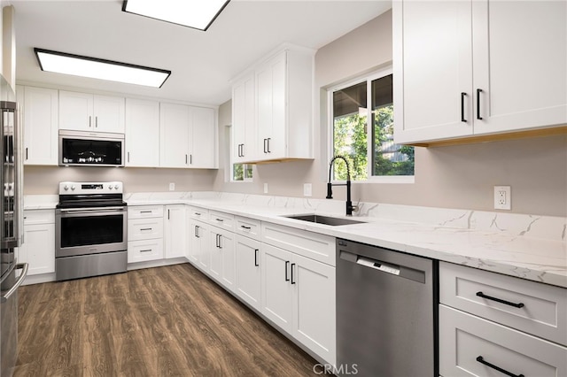 kitchen with stainless steel appliances, dark wood-style floors, a sink, white cabinetry, and light stone counters