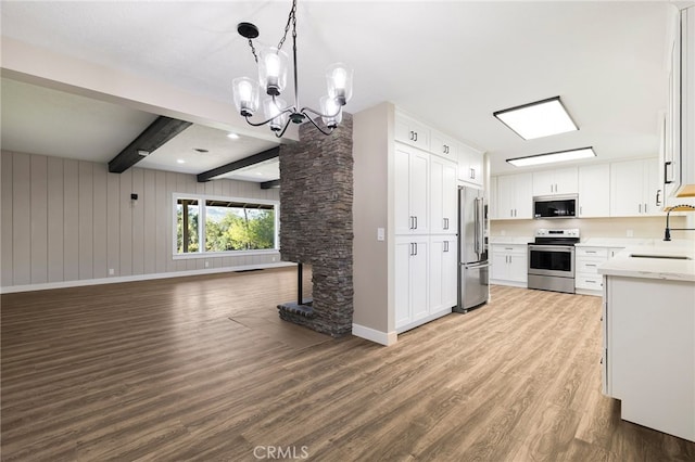 kitchen featuring stainless steel appliances, a sink, open floor plan, wood finished floors, and light countertops