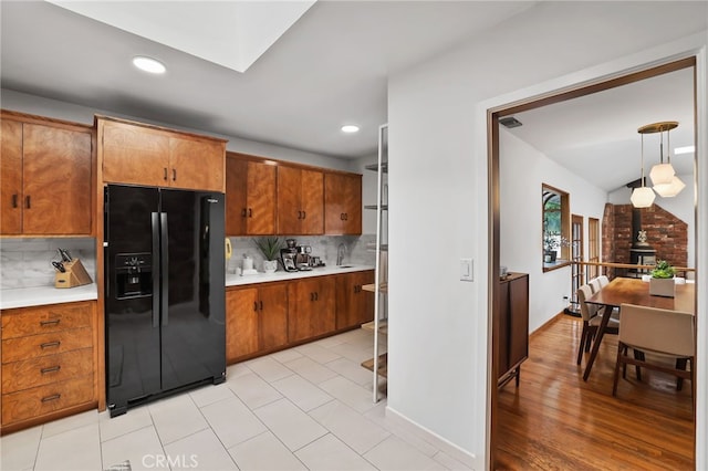 kitchen with black fridge with ice dispenser, light countertops, backsplash, and brown cabinets