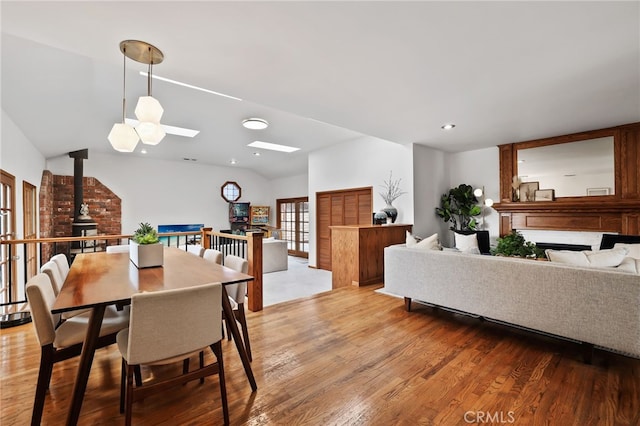 dining room with light wood-style flooring, recessed lighting, a wood stove, and vaulted ceiling with skylight