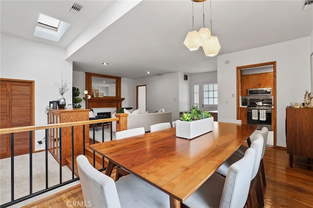 dining space featuring a fireplace, wood finished floors, visible vents, and a skylight