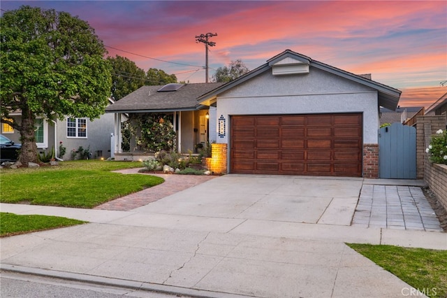 ranch-style home featuring a gate, driveway, a garage, a yard, and stucco siding