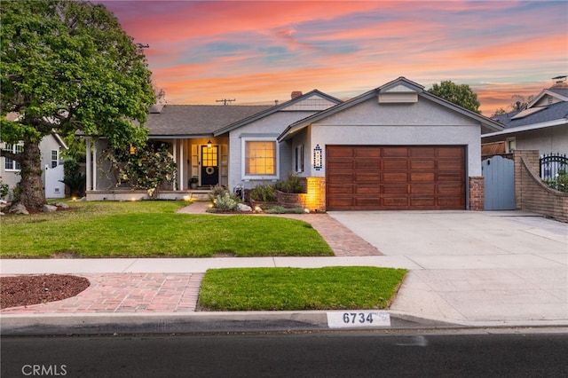 ranch-style home featuring a gate, a front lawn, driveway, an attached garage, and stucco siding