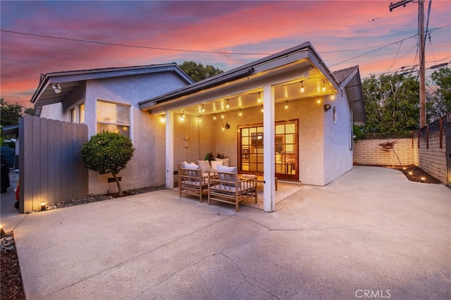 back of house at dusk with stucco siding, fence, an outdoor living space, and a patio area