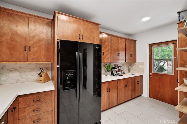 kitchen with a sink, tasteful backsplash, black refrigerator with ice dispenser, brown cabinets, and open shelves