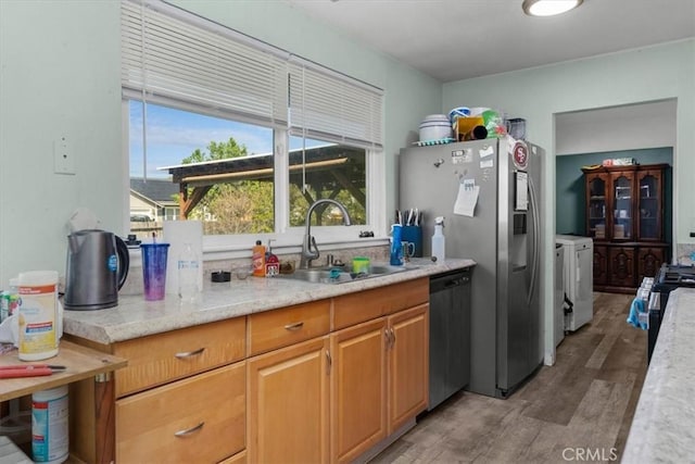 kitchen with a sink, stainless steel gas range, washing machine and dryer, light wood-type flooring, and dishwasher