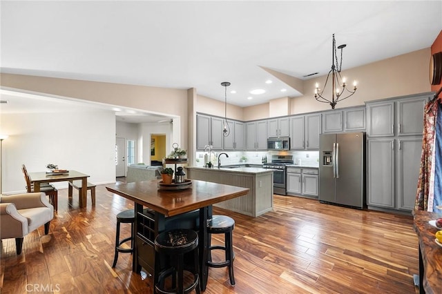 kitchen with a sink, appliances with stainless steel finishes, wood finished floors, and gray cabinetry