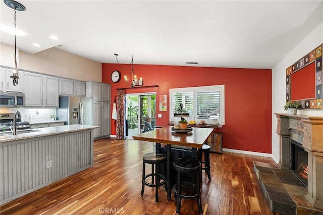 dining area with dark wood-type flooring, baseboards, lofted ceiling, and a warm lit fireplace