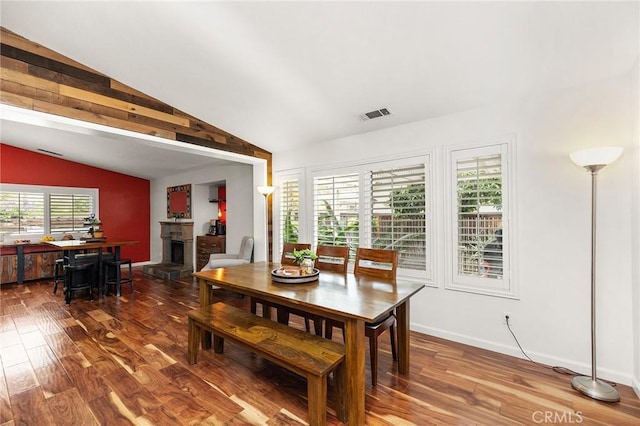 dining area with visible vents, a fireplace with raised hearth, lofted ceiling, and wood finished floors