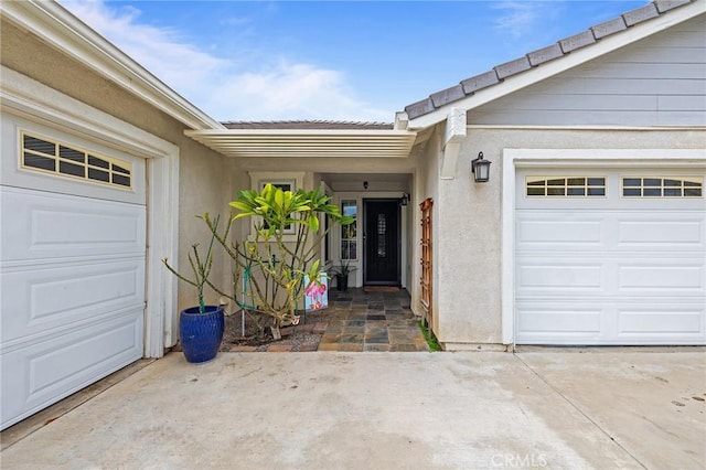 property entrance featuring concrete driveway, stucco siding, an attached garage, and a tiled roof